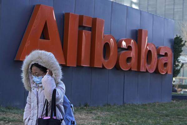 FILE - A woman wearing a face mask walks by the offices of Chinese e-commerce firm Alibaba in Beijing on Dec. 13, 2021.    Alibaba Group on Thursday, Nov. 17, 2022,  posted net losses and missed market expectations for revenue in its quarter ended September amid a slowing economy and depressed consumer sentiment.   (AP Photo/Andy Wong, File)