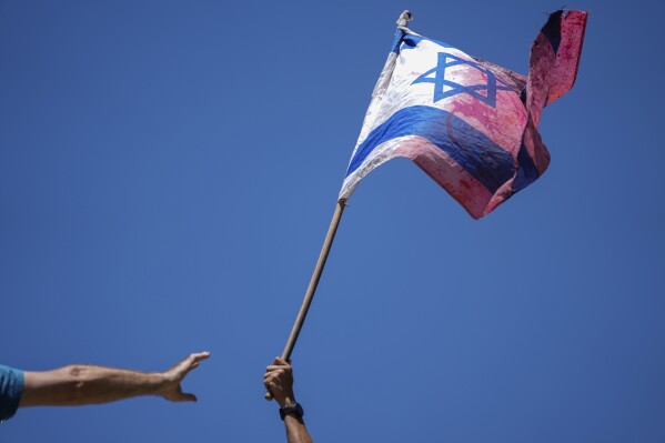 A demonstrator waves a colored Israeli flag during a protest against plans by Prime Minister Benjamin Netanyahu's government to overhaul the judicial system, outside the Knesset, Israel's parliament, in Jerusalem, Monday, July 24, 2023. The demonstration came hours before parliament was set to vote on a key part of the plan. (AP Photo/Ariel Schalit)