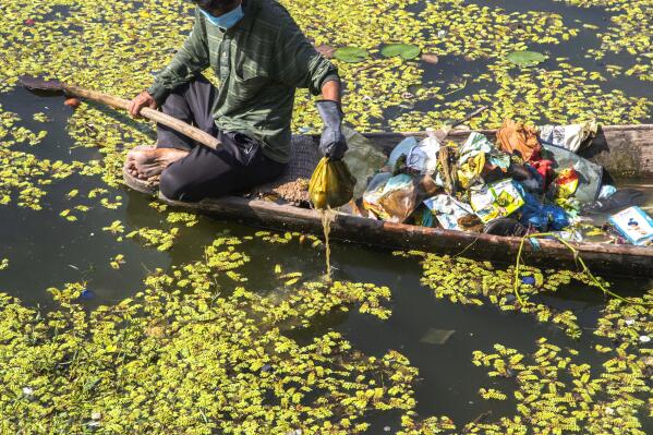 A Kashmiri boatman employed by the Lakes and Waterways Development Authority removes garbage from the Dal Lake in Srinagar, Indian controlled Kashmir, Sept. 14, 2021. Dal Lake appears pristine in the area where hundreds of exquisitely decorated houseboats bob on its surface for rent by tourists and honeymooners. But farther from shore, the lake is a mixture of mossy swamps, thick weeds, trash-strewn patches and floating gardens made from rafts of reeds. (AP Photo/Mukhtar Khan)