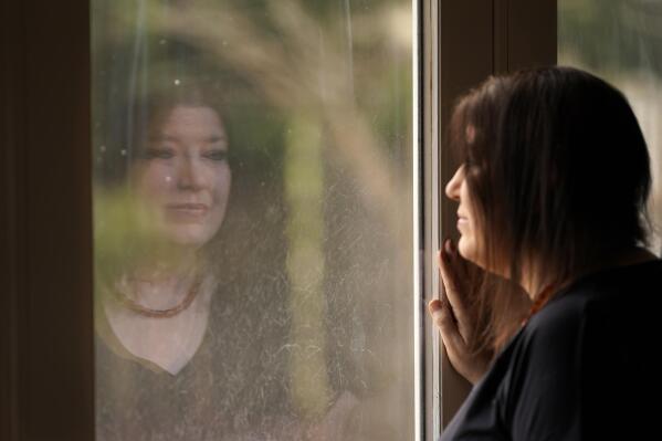 CORRECTS TO KARI, NOT KERI - Kari Wegg is reflected in a sliding glass door as she looks outside her home in Westfield, Ind., on Monday, March 22, 2021. The Indiana nurse came down with COVID-19 in the summer of 2020; her condition spiraled downward, and her life was saved only by grace of a double lung transplant. The road to normal is a long one, but she's bolstered by the love and support of her husband and sons, and by her own indomitable spirit. (AP Photo/Charles Rex Arbogast)