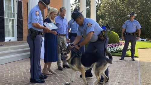 Police K-9 Rex struggles with his handler Trooper First Class Gustabo Deanda during a graduation ceremony, Thursday, July, 13, 2023, at the governor's mansion in Atlanta. Georgia first lady Marty Kemp, second from left, helped rescue Rex from an animal shelter last year and arrange for him to enter training with the Georgia Department of Public Safety. Georgia Gov. Brian Kemp, third from left, watches. (AP Photo/Jeff Amy)