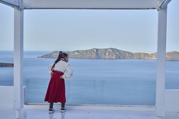 A woman from China looks on from a caldera at Firostefani, as in the background stands the island of Therasia, while authorities are taking emergency measures in response to intense seismic activity on the popular Aegean Sea holiday island of Santorini, southern Greece, Tuesday, Feb. 4, 2025. (AP Photo/Petros Giannakouris)