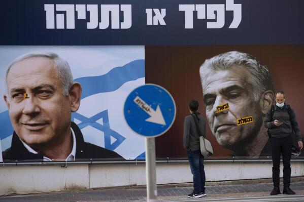 FILE - In this March 14, 2021 file photo, people stand in front of an election campaign billboard for the Likud party showing a portrait of its leader Prime Minister Benjamin Netanyahu, left, and opposition party leader Yair Lapid, in Ramat Gan, Israel. Israel’s President Reuven Rivlin has tapped Lapid to form a new government, a step that could lead to the end of Netanyahu’s lengthy rule. (AP Photo/Oded Balilty, File)