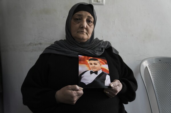 Rawiya Halhouli holds a photo of her slain son Rami Halhouli, in their house in Shuafat refugee camp in east Jerusalem, Sunday, March 17, 2024. Halhouli, 12, was fatally by an Israeli police officer while launching a firework on March 12. (AP Photo/Mahmoud Illean)