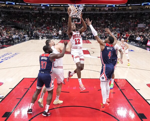 Chicago Bulls' Ayo Dosunmu (12) drives to the basket between Washington Wizards' Eugene Omoruyi (97) and Jared Butler (4) during the first half of an NBA basketball game Saturday, March 16, 2024, in Chicago. (AP Photo/Charles Rex Arbogast)