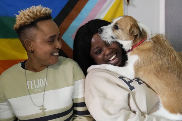 Ella Anthony, left, and her partner Doris Ezuruike Chinons pose for a photo with their dog Paddy, during an interview in their house in Passo Corese, near Rome, Monday, March 11, 2024. Knowing that she faced a possible prison term since Nigeria criminalizes same-sex relationships, Anthony fled with her partner to Libya in 2014 and then Italy, where they both won asylum. Their claim? That they had a well-founded fear of anti-LGBTQ+ persecution back home. (AP Photo/Alessandra Tarantino)