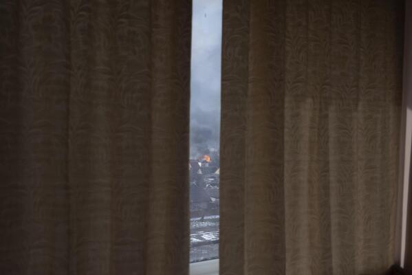 Seen through partially drawn curtains a house burns after shelling in Mariupol, Ukraine, Saturday, March 12, 2022. (AP Photo/Mstyslav Chernov)