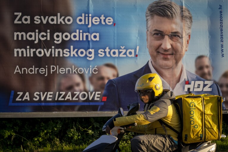 A delivery man waits for green light on a street in front of an election poster in Zagreb, Croatia, Sunday, April 14, 2024. Croatia this week holds a parliamentary election following a campaign that was marked by heated exchanges between the country's two top officials, creating a political crisis in the Balkan country, a European Union and NATO member state. (AP Photo/Darko Bandic)