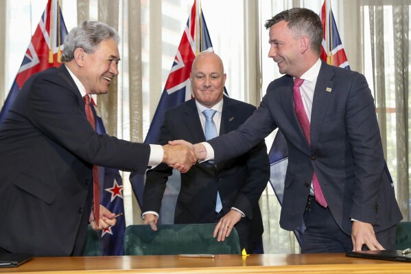 New Zealand Prime Minister elect Christopher Luxon, centre, watches as his coalition partners, New Zealand First leader Winston Peters, left, and ACT leader David Seymour shake hands following a signing ceremony in Wellington, New Zealand, Friday, Nov. 24, 2023. New Zealanders can expect tax cuts, more police on the streets and reductions to government bureaucracy, according to the three leaders who signed an agreement Friday to form a new government. The coalition deal ended nearly six weeks of intense negotiations after New Zealand held a general election on Oct. 14. (Mark Mitchell/NZ Herald via AP)