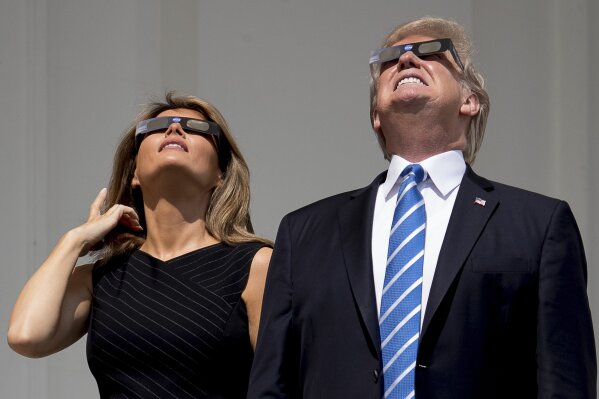 FILE - In this Aug. 21, 2017, file photo, President Donald Trump and first lady Melania Trump wear protective glasses as they view the solar eclipse at the White House in Washington. Trump's comment about injecting disinfectant to fight coronavirus is just the latest in a long list of comments and actions that run contrary to mainstream science. He's gone against scientific and medical advice by staring at an eclipse without protection, calling climate change a hoax and saying wind turbines cause cancer.  (AP Photo/Andrew Harnik, File)