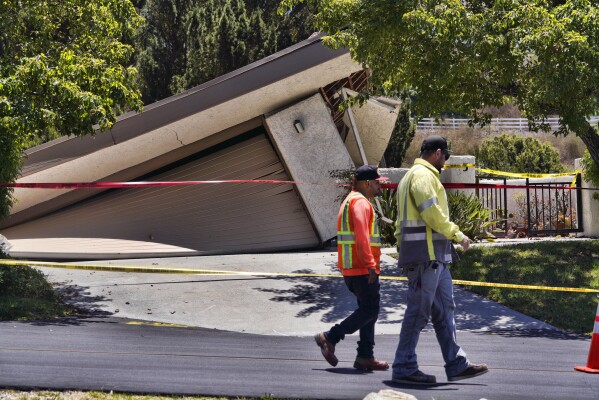 City employees walk past a damaged house teetering over a ravine in Rolling Hills Estates on the Palos Verdes Peninsula in Los Angeles County, on Monday, July 10, 2023. A dozen homes torn apart by earth movement on Southern California's Palos Verdes Peninsula during the weekend are likely to fall into an adjacent canyon. The homes iwere hastily evacuated by firefighters Saturday when cracks began appearing in structures and the ground. (AP Photo/Richard Vogel)