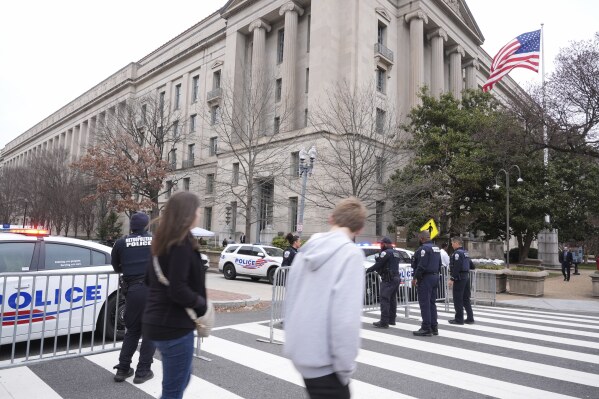 Pedestrians walk as police secure the area around the Justice Department before President Donald Trump speaks Friday, March 14, 2025, in Washington. (AP Photo/Jacquelyn Martin)