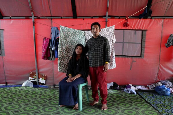 Samira, left, and her husband, Akram Ullah, both ethnic Rohingya refugees, pose for a photograph at a temporary shelter in Meulaboh, Indonesia, on Thursday, April 4, 2024. They were among 75 people rescued in March from atop the overturned hull of a boat that capsized off Indonesia's coast. Dozens of other Rohingya refugees died. (AP Photo/Reza Saifullah)