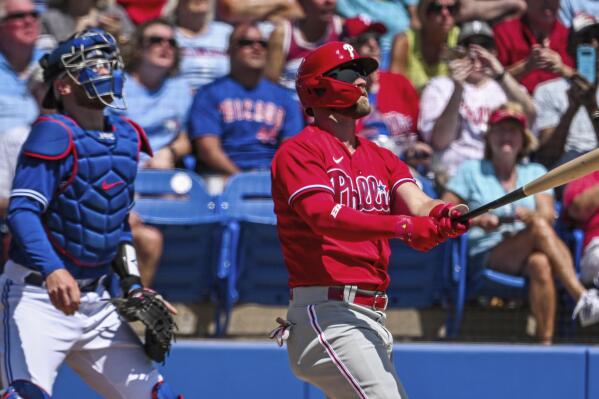 Toronto Blue Jays catcher Danny Jansen, left, looks on as Philadelphia Phillies' Bryce Harper hits a solo home run during the first inning of a spring training baseball game against the Philadelphia Phillies in Dunedin, Fla., Sunday, March 27, 2022. (Steve Nesius/The Canadian Press via AP)