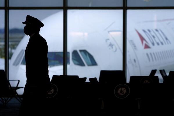 FILE - A Delta Airlines pilot wears a face mask as he walks through a terminal at Hartsfield-Jackson International Airport in Atlanta, on Thursday, Feb. 18, 2021. Airlines executives told legislators on Wednesday, Dec. 15 they are having trouble hiring pilots, flight attendants and other personnel, and that’s part of what is causing canceled flights and scrapping of service to some airports.  (AP Photo/Charlie Riedel, File)