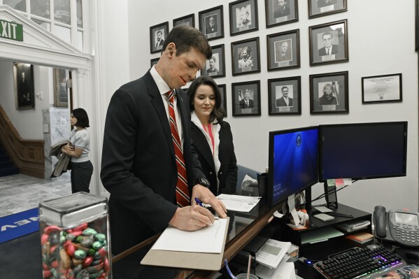 Republican U.S. Senatorial candidate Sam Brown, with his wife Amy Brown, signs in at the Secretary of State office as he arrives to files his paperwork to run for the Senate, Thursday, March 14, 2024, at the State Capitol in Carson City, Nev. Brown is seeking to replace incumbent U.S. Sen. Jacky Rosen. (AP Photo/Andy Barron)