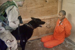 This undated still photo made available by The Washington Post on May 21, 2004, shows a U.S. soldier, who was identified in a military court-martial as Sgt. Michael J. Smith, holding a dog in front an Iraqi detainee at Abu Ghraib prison on the outskirts of Baghdad. A federal judge has again refused to dismiss a lawsuit brought by former Abu Ghraib inmates against a military contractor they accuse of being complicit in torture at the infamous Iraqi prison. The horrific mistreatment of prisoners there two decades ago sparked international outrage when photos became public of smiling U.S. soldiers posing in front of abused prisoners. (The Washington Post via AP)