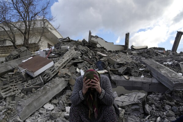 A woman sits on the rubble as emergency rescue teams search for people under the remains of earthquake destroyed buildings in Nurdagi town on the outskirts of Osmaniye city southern Turkey, Tuesday, Feb. 7, 2023. (AP Photo/Khalil Hamra)