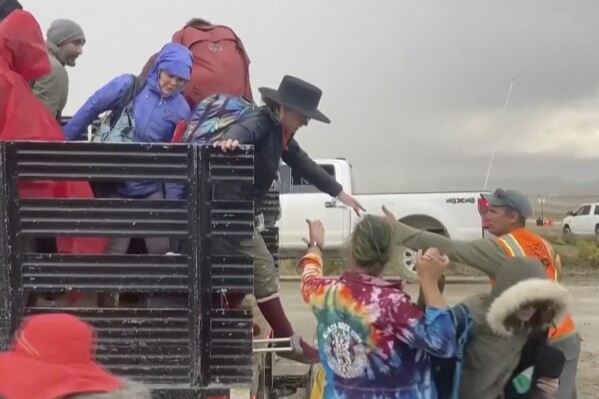 CORRECTS THAT THE SOURCE IS STRINGR, NOT REBECCA BARGER - In this image from video provided by Stringr, festival goers are helped off a truck from the Burning Man festival site in Black Rock, Nev., on Monday, Sept. 4, 2023. An unusual late-summer storm stranded thousands at the week-long event. (Stringr via AP)