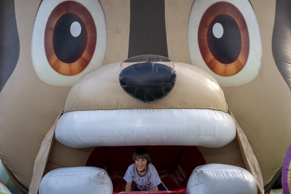 A child peers from a cartoon character shaped inflatable slide at a fair in Hagioaica, Romania, Thursday, Sept. 14, 2023. For many families in poorer areas of the country, Romania's autumn fairs, like the Titu Fair, are one of the very few still affordable entertainment events of the year. (AP Photo/Andreea Alexandru)