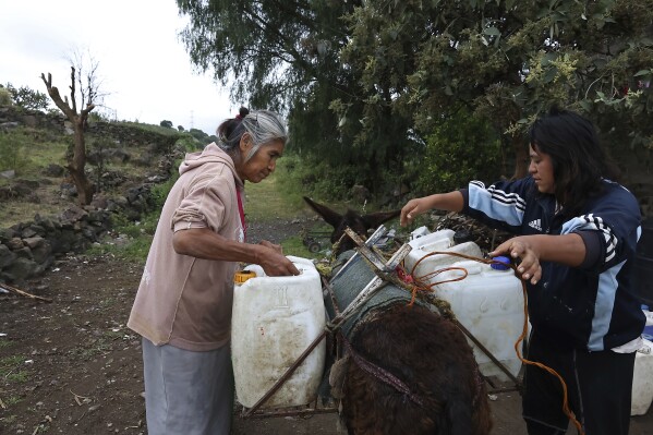 Emilia Segura, left, and her daughter Cecilia Rivera Segura arrange containers after filling them with water at a free, public well in Pueblo Santa Cruz Acalpixca, Xochimilco, on the outskirts of Mexico City, Saturday, Oct. 7, 2023. Segura, 62, has been selling water daily for over a decade with the help of her four donkeys. The system which provides the capital with over a quarter of its drinking water is 44% lower than it should be and have set a new record, according to government figures, and authorities have begun cutting water to the city. (AP Photo/Ginnette Riquelme)