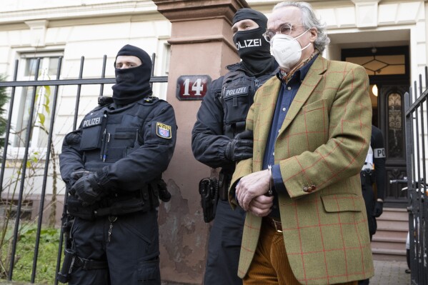FILE - Masked police officers lead Heinrich XIII Prince Reuss, right, to a police vehicle during a raid against so-called 'Reich citizens' in Frankfurt, Germany, Wednesday, Dec. 7, 2022. Nine suspects, among them a self-styled prince and a former far-right lawmaker, will go on trial next month in the most prominent of three cases connected to an alleged plot to topple the German government that came to light in late 2022, a court said Tuesday, April 2, 2024. (Boris Roessler/dpa via AP, File)