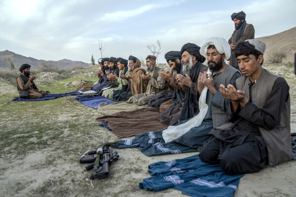 Taliban fighters and other men pray in a cemetery in a village in a remote region of Afghanistan, on Friday, Feb. 24, 2023. A farmer, his wife and their five children killed during a Sept. 5, 2019, night raid by U.S. forces, were buried here, where generations of their kin had been laid to rest. (AP Photo/Ebrahim Noroozi)