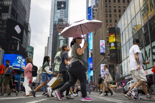 FILE - A pedestrian uses an umbrella to shield against the sun while passing through Times Square as temperatures rise, July 27, 2023, in New York. At about summer's halfway point, the record-breaking heat and weather extremes are both unprecedented and unsurprising, hellish yet boring in some ways, scientists say. (AP Photo/John Minchillo, File)