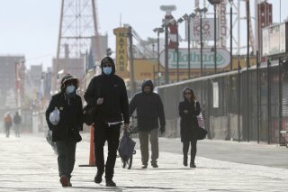 Pedestrians enjoy the warm weather on the boardwalk at Coney Island in New York, Sunday, April 12, 2020. Amid some signs of hope that the coronavirus infection rate is plateauing, New York is still wrapping up its worst week in deaths so far since the outbreak began. (AP Photo/Seth Wenig)