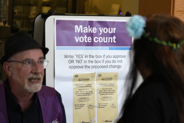 A polling place volunteer, left, assists a woman at a polling place in Redfern as Australians cast their final votes in Sydney, Saturday, Oct. 14, 2023, in their first referendum in a generation that aims to tackle Indigenous disadvantage by enshrining in the constitution a new advocacy committee. The prospect of an Indigenous Voice to Parliament has bitterly divided Australia's Indigenous minority as well as the wider community. (AP Photo/Rick Rycroft)