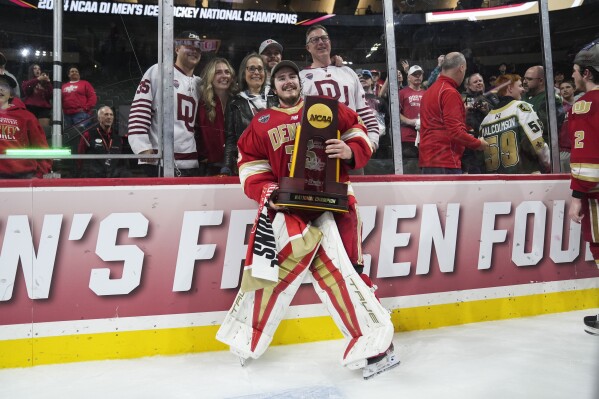 Denver goaltender Matt Davis (35) poses with the championship trophy, with his family behind him, after defeating Boston College in the championship game of the Frozen Four NCAA college hockey tournament Saturday, April 13, 2024, in St. Paul, Minn. Denver won 2-0 to win the national championship. (AP Photo/Abbie Parr)