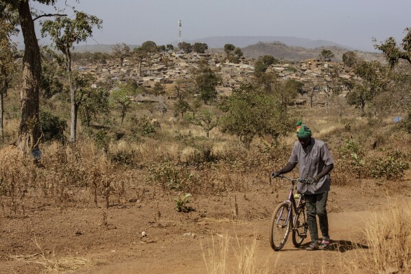 A man walks with his bike with a view of a town built near a gold mining site in the Kedougou region of Senegal on Thursday, Jan. 16, 2025. (AP Photo/Annika Hammerschlag)