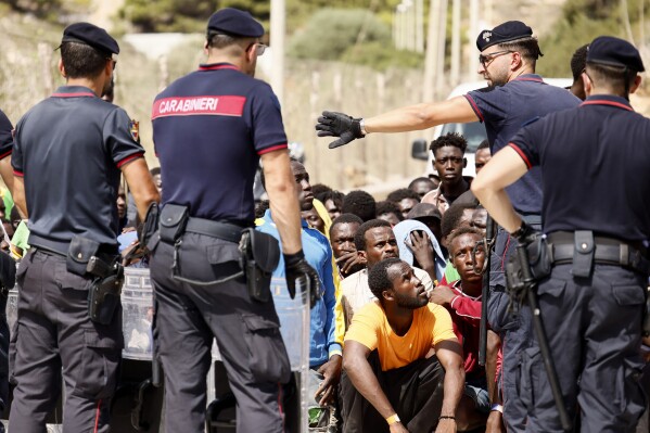 Italian carabinieri police speak to migrants protesting at a reception center on the Sicilian island of Lampedusa, southern Italy, Saturday, Sept. 16, 2023. Thousands of migrants and refugees have landed on the Italian island of Lampedusa this week after crossing the Mediterranean Sea on small unseaworthy boats from Tunisia, overwhelming local authorities and aid organizations. (Cecilia Fabiano/LaPresse via AP)