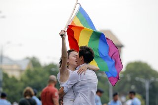 
              FILE - In this Saturday, June 9, 2018 file photo, two girls kiss holding a rainbow flag during the gay pride parade in Bucharest, Romania. Romania's top court has ruled that gay couples should have the same family rights as heterosexuals, a judgment that comes before a referendum seeking to ban same-sex marriage. The Constitutional Court has ruled that same-sex couples have the same rights to a private and family life as heterosexuals. Teodora Ion-Rotaru, of the gay rights group Accept, told The Associated Press on Friday, Sept. 28 the ruling was "extremely important." (AP Photo/Vadim Ghirda, file)
            
