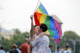 FILE - In this Saturday, June 9, 2018 file photo, two girls kiss holding a rainbow flag during the gay pride parade in Bucharest, Romania. Romania's top court has ruled that gay couples should have the same family rights as heterosexuals, a judgment that comes before a referendum seeking to ban same-sex marriage. The Constitutional Court has ruled that same-sex couples have the same rights to a private and family life as heterosexuals. Teodora Ion-Rotaru, of the gay rights group Accept, told The Associated Press on Friday, Sept. 28 the ruling was "extremely important." (AP Photo/Vadim Ghirda, file)