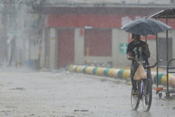 A man rides his bicycle under the rain brought by Hurricane Iota, in La Lima, Honduras, Tuesday, Nov. 17, 2020. Hurricane Iota tore across Nicaragua on Tuesday, hours after roaring ashore as a Category 4 storm along almost exactly the same stretch of the Caribbean coast that was recently devastated by an equally powerful hurricane. (AP Photo/Delmer Martinez)
