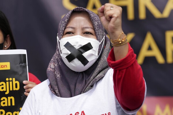 A masked activist shouts slogans during a protest and hunger strike demanding the parliament to pass a bill to protect domestic workers outside the parliament in Jakarta, Indonesia Monday, Aug. 14, 2023. Indonesian domestic workers and activists began a hunger strike on Monday to protest against the parliament's delay in passing a bill to protect domestic workers. (AP Photo/Tatan Syuflana)