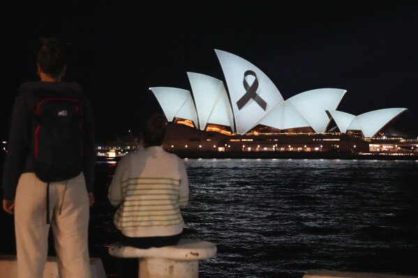 People look as the Sydney Opera House is illuminated with a black ribbon Monday, April 15, 2024, as part of the national day of mourning following the stabbing deaths at a shopping mall in Sydney's East on Saturday. Australian police are examining why a lone assailant who stabbed multiple people to death in a busy Sydney shopping mall and injured more than a dozen others targeted women while avoiding men. (AP Photo/Mark Baker)