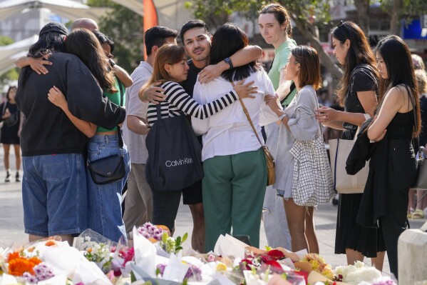 A group of people react after placing flowers as a tribute near a crime scene at Bondi Junction in Sydney, Monday, April 15, 2024, after several people were stabbed to death at a shopping on April 13. Australian police are examining why a lone assailant who stabbed several people to death in a busy Sydney shopping mall and injured more than a dozen others targeted women while avoiding men. (AP Photo/Mark Baker)