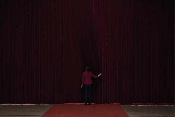 A hostess closes a curtain after delegates attending the opening session of the Chinese People's Political Consultative Conference at the Great Hall of the People in Beijing, Tuesday, March 4, 2025. (AP Photo/Andy Wong)