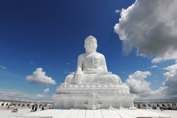 Laborers work while visitors stand below the sitting Maravijaya Buddha marble statue, Friday, July 21, 2023, in Naypyitaw, Myanmar. The Maravijaya Buddha statue is said to be the world’s highest sitting marble Buddha image according to local media. (AP Photo/Aung Shine Oo)