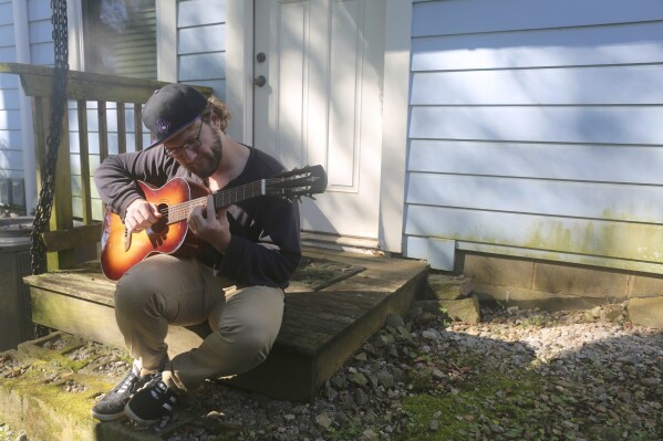 Camera assistant Alex Buhlig plays his guitar outside his Atlanta apartment on Oct. 18, 2023. With the actors' strike still ongoing and filming largely shut down, Buhlig has been teaching guitar lessons to make ends meet. (AP Photo/R.J. Rico)
