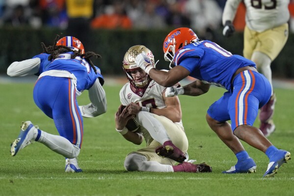 Florida cornerback Jaydon Hill, left, and safety Bryce Thornton, right, hit Florida State quarterback Tate Rodemaker, center, as he slides during the second half of an NCAA college football game, Saturday, Nov. 25, 2023, in Gainesville, Fla. Hill was charged with targeting and was ejected. (AP Photo/John Raoux)