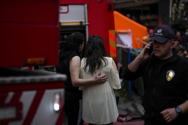 Two women gather as firefighters and emergency teams work in the aftermath of a fire in a nightclub in Istanbul, Turkey, Tuesday, April 2, 2024. A fire at an Istanbul nightclub during renovations on Tuesday killed at least 29 people, officials and reports said. Several people, including managers of the club, were detained for questioning. (AP Photo/Khalil Hamra)