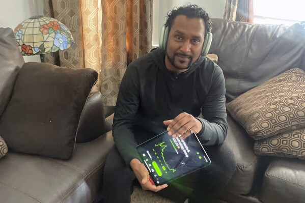 In this photo provided by Richard Persaud, he holds a tablet showing the stock chart of Trump Media & Technology, at his home in Schenectady, N.Y., on Wednesday, April 24, 2024. “I don’t know which direction the stock is going,” says Persaud while checking his iPhone amid a recent surge. “It’s so unbelievably overvalued.” (Courtesy Richard Persaud via AP)