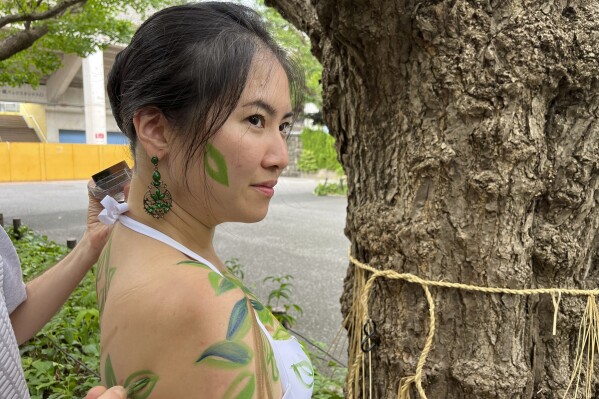 Miho Nakashima has her body painted like a tree by artist Andy Boerger during a public protest on Sunday, Aug. 27, 2023, to point out that 100-year-old trees in the Jingu Gaien park area in Tokyo, Japan, could be cut down under a disputed development plan. (AP Photo/Stephen Wade)