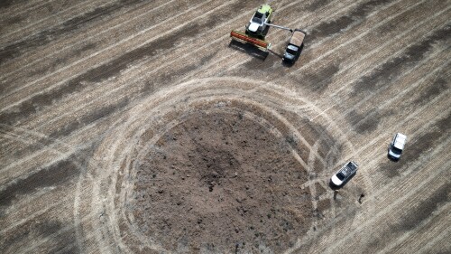 FILE - A farmer harvests crops in a field ten kilometers from the front line, around a crater left by a Russian rocket in the foreground, in Dnipropetrovsk region, Ukraine, on July 4, 2022. Agreements that the UN and Turkey negotiated with Ukraine and Russia will allow food and fertilizer to flow from warring nations to parts of the world where millions go hungry has eased concerns about global food security.  But they face growing risks.  Moscow has stepped up its rhetoric, saying it may not extend the deal, which expires on Monday, July 17, 2023, unless its demands are met.  (AP Photo/Efrem Lukatsky, File)