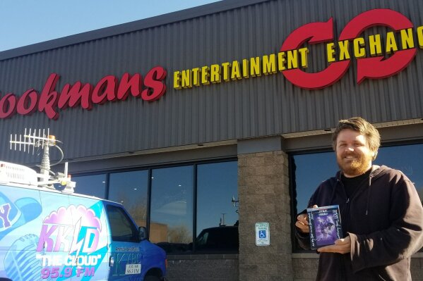 In this photo taken in Jan. 11, 2020, Bookmans Entertainment Exchange general manager Micheil Salmons stands in front of the store in Flagstaff, Ariz., holding a DVD autographed by Star Wars actor Mark Hamill. Workers at Bookmans returned to Hamill a “Star Wars: A New Hope” soundtrack that had been a gift from film composer John Williams. (Scott Buffon/Arizona Daily Sun via AP)