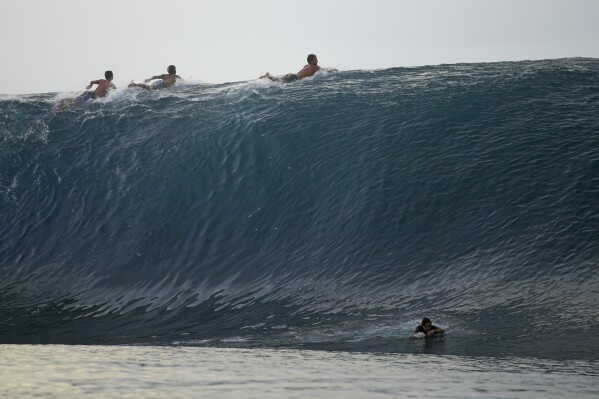 Surfers paddle over the top of a wave in Teahupo'o, Tahiti, French Polynesia, Sunday, Jan. 13, 2024. (AP Photo/Daniel Cole)