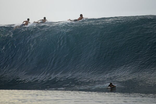 Surfers paddle on the waves in Te Aupoo, Tahiti, French Polynesia, Sunday, January 13, 2024. (AP Photo/Daniel Cole)